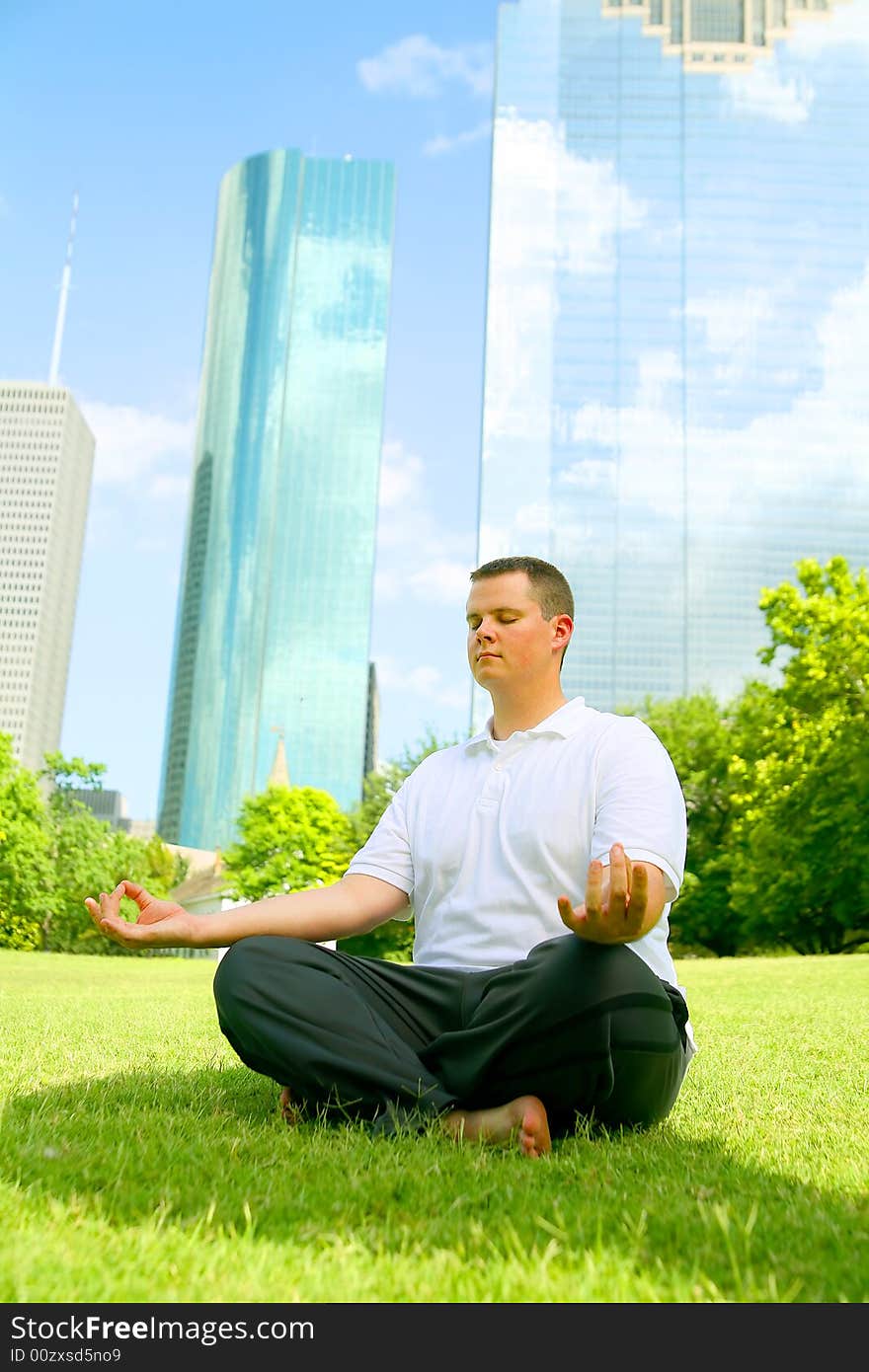 Handsome caucasian man meditate outdoor in a park with downtown building in the background. concept for yoga or wellbeing. Handsome caucasian man meditate outdoor in a park with downtown building in the background. concept for yoga or wellbeing