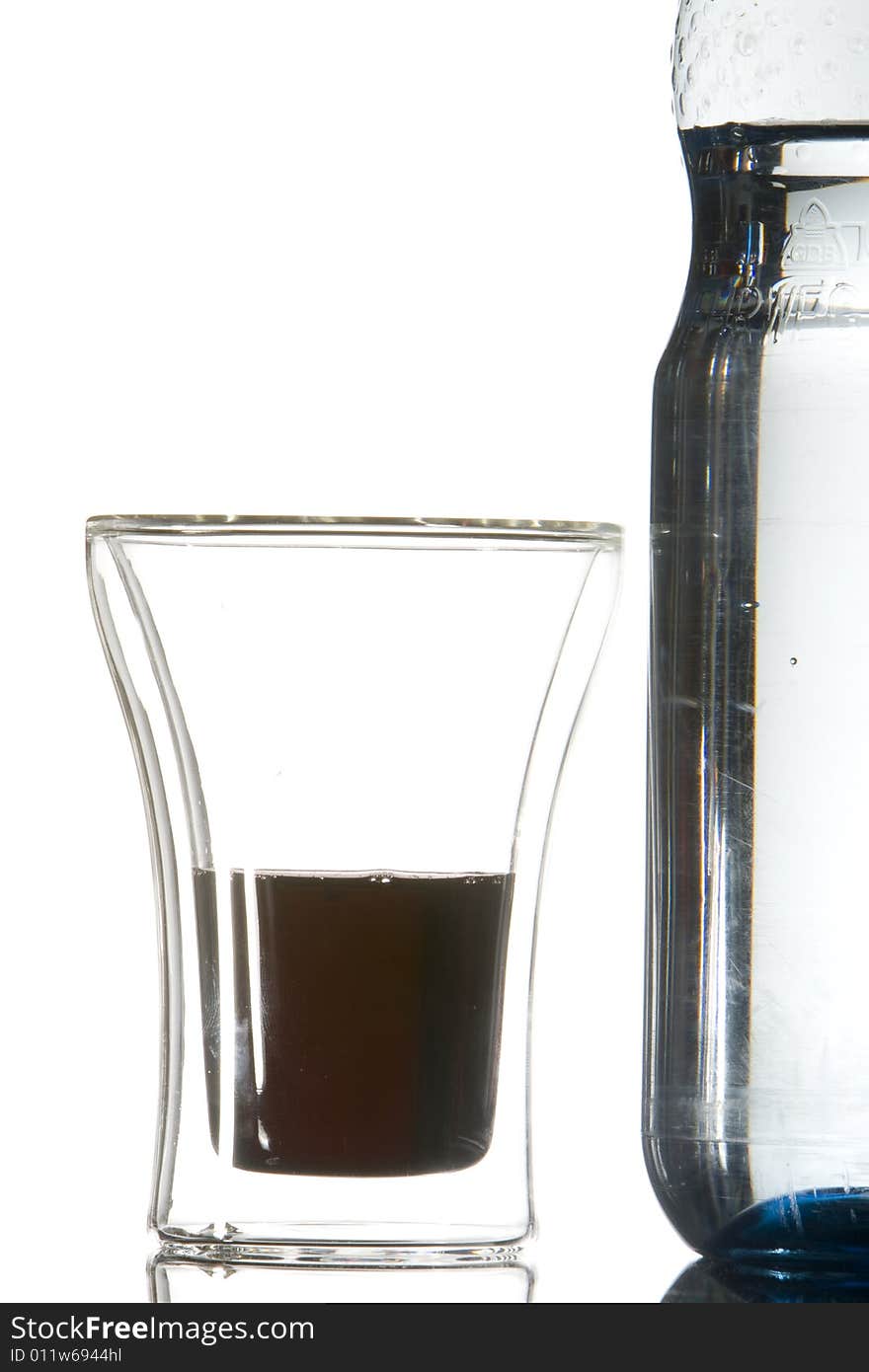 A waterbottle and a glass with a dark-red drink. A waterbottle and a glass with a dark-red drink