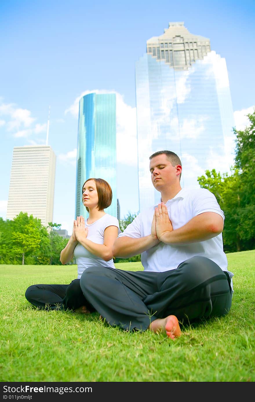 Young caucasian couple meditate outdoor in a park with downtown building on the background. concept for yoga, family activity or wellbeing. Young caucasian couple meditate outdoor in a park with downtown building on the background. concept for yoga, family activity or wellbeing