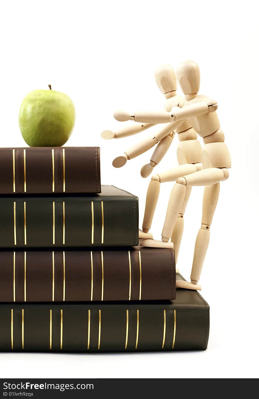 Wooden figurine on a stack of books going up for an apple