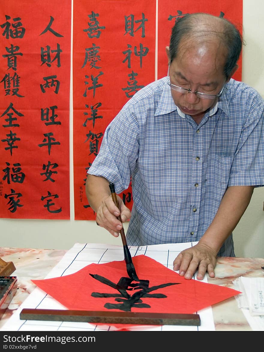 Man writing Chinese calligraphy on red paper. Man writing Chinese calligraphy on red paper