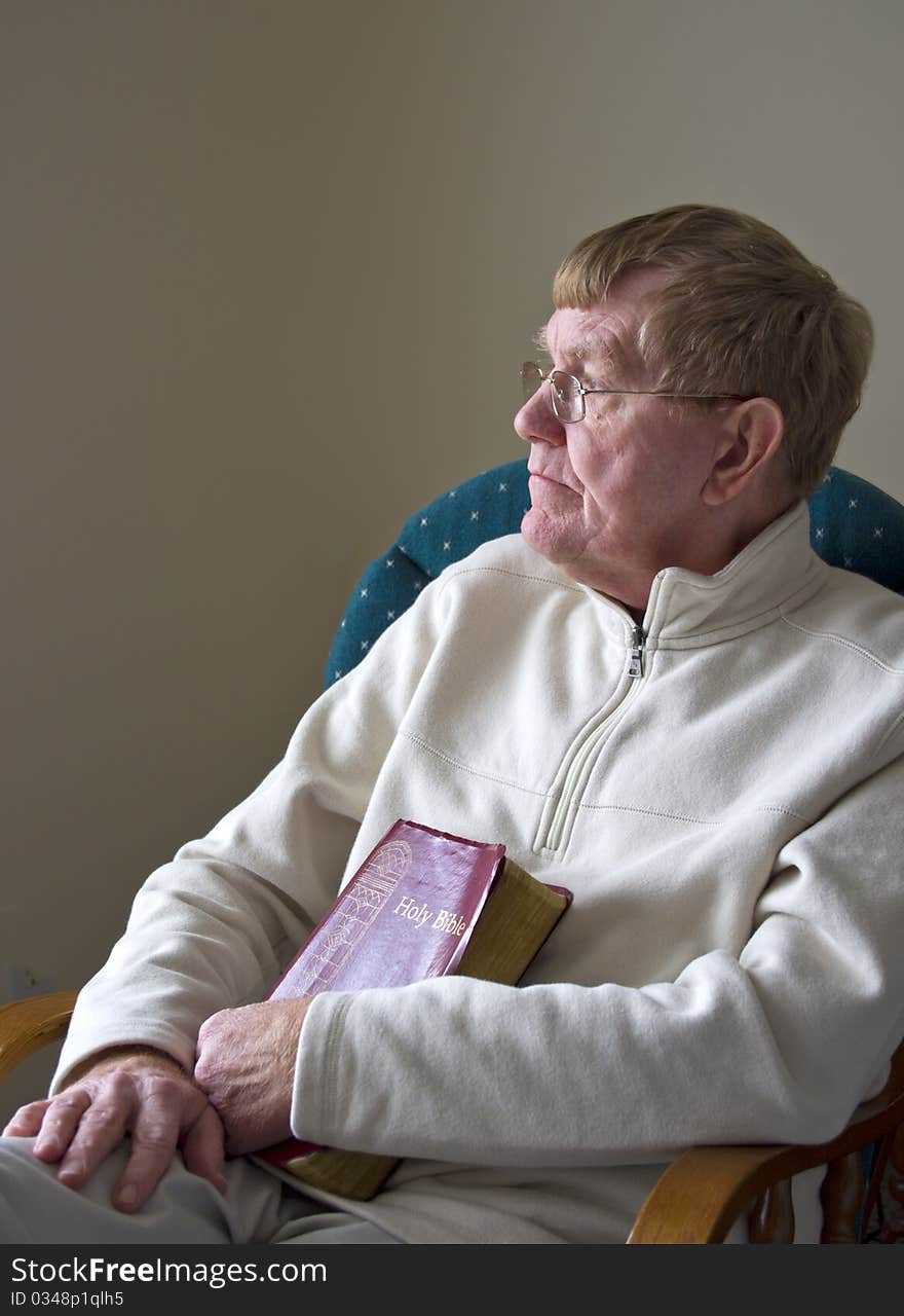 An older man sitting in a chair with his Bible. An older man sitting in a chair with his Bible.