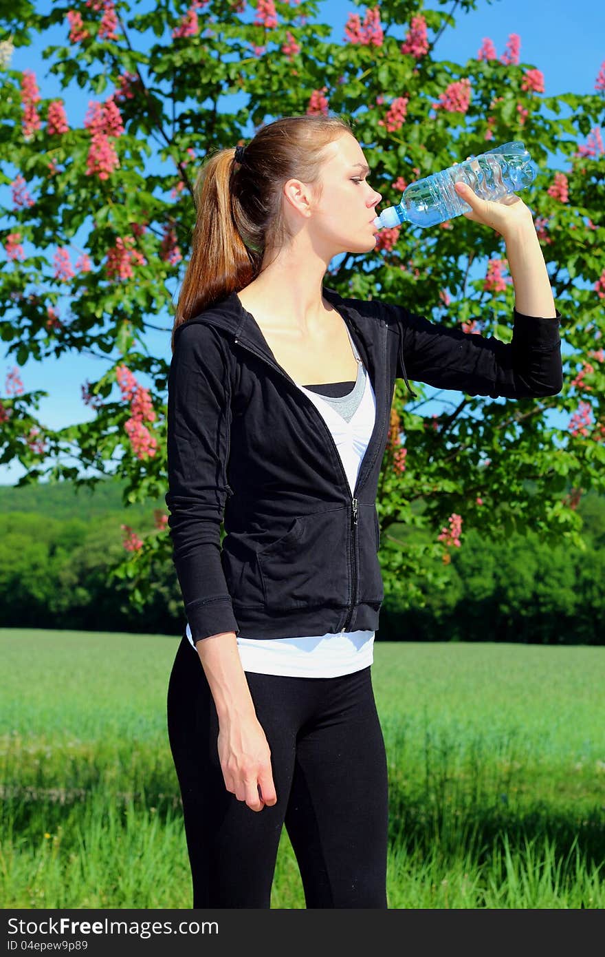 Sportive young woman drinking water in the nature