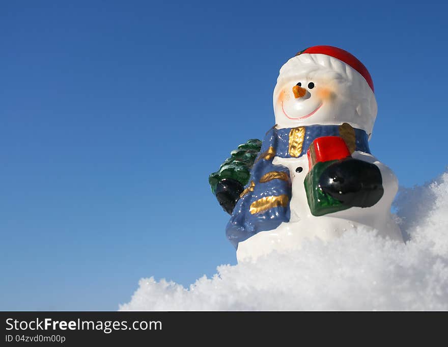 Smiling snowman figurine in snow with blue background