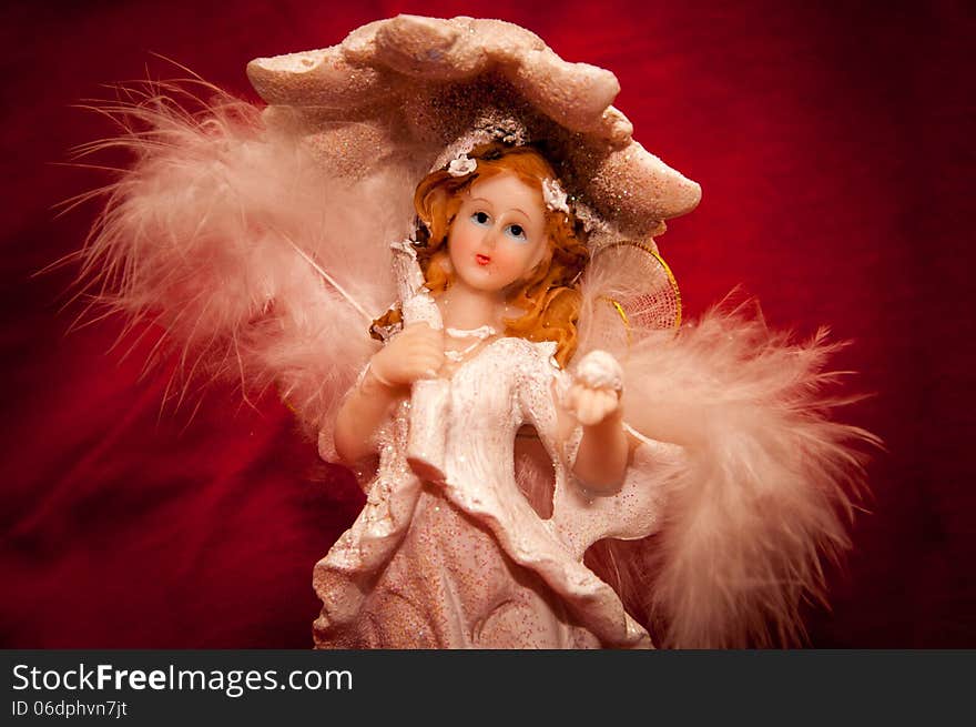 Portrait of a handmade angel figurine on a stylish red background.