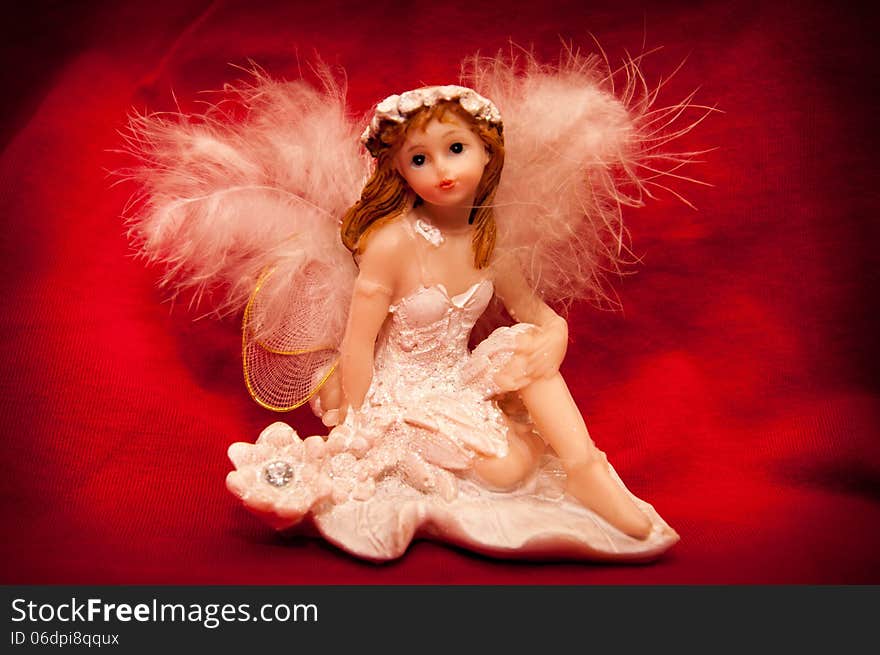 Portrait of a handmade angel figurine on a stylish red background.