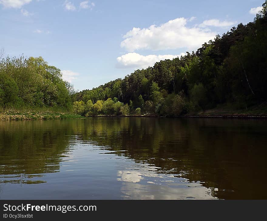 Calm bend of river with forest on banks clouds and reflection in water