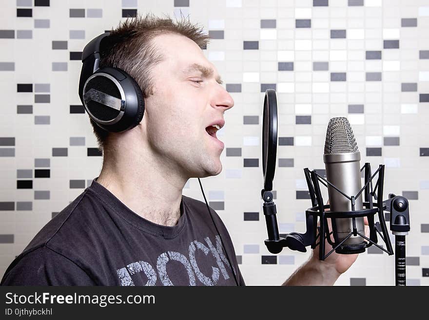 A young guy singer and rock musician sings in a studio condenser microphone in headphones in a recording studio