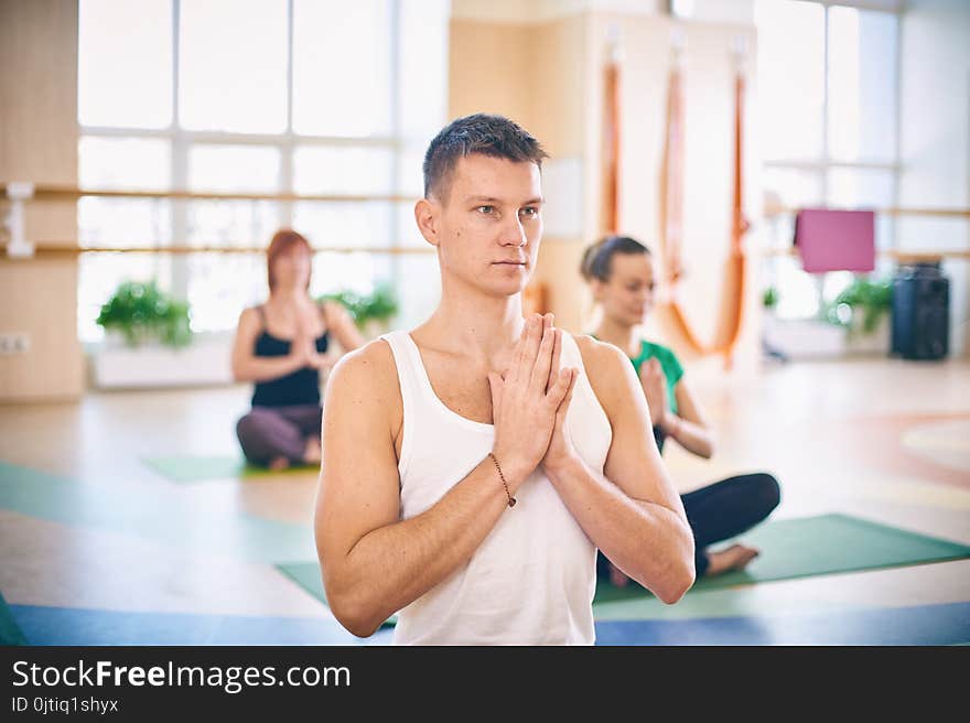 Group of young sporty people practicing yoga lesson with instructor, sitting in Padmasana exercise, Lotus pose with folded hands in namaste in yoga studio