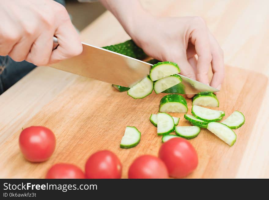 Close-up of female hands cut into fresh cut cucumbers on a wooden cutting board next to pink tomatoes. The concept of homemade vegetarian cuisine and healthy eating and lifestyle.