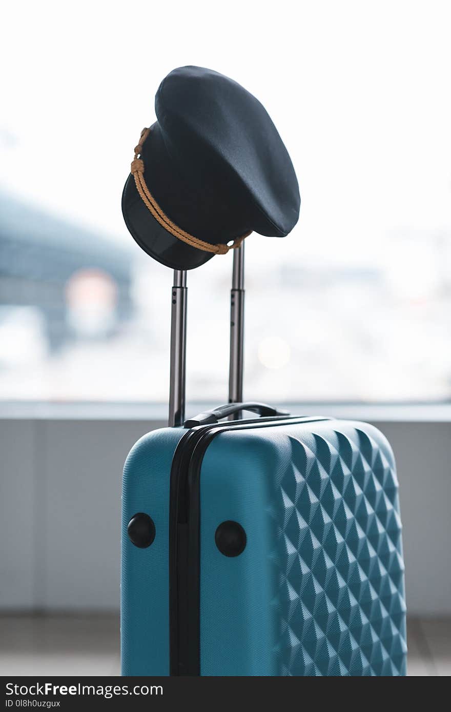 pilot cap hanging on handle of suitcase at airport