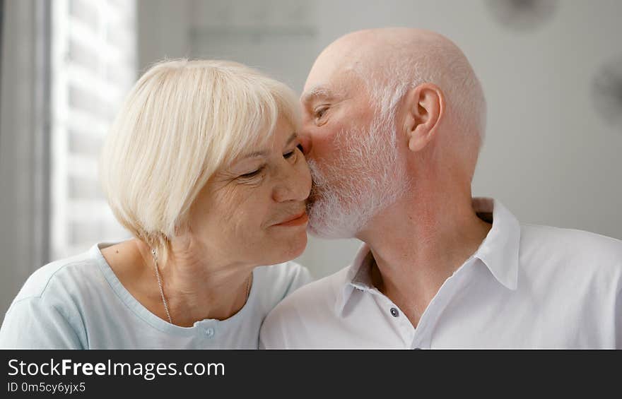 Portrait of happy senior couple at home. Senior man expresses his emotions and kisses his wife