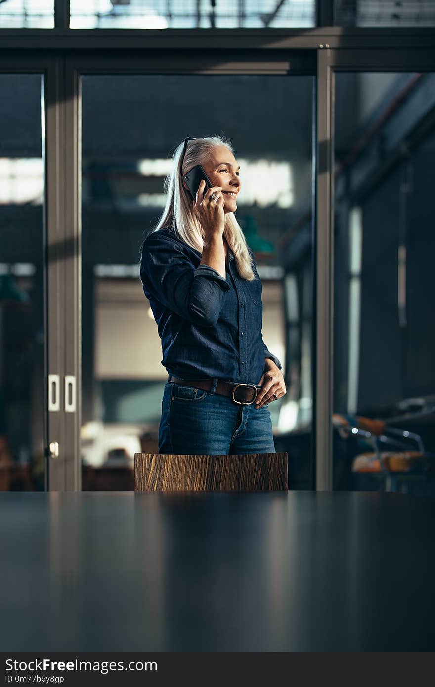 Smiling mature businesswoman in casuals talking on cell phone. Senior female executive in office making a phone call. Smiling mature businesswoman in casuals talking on cell phone. Senior female executive in office making a phone call.