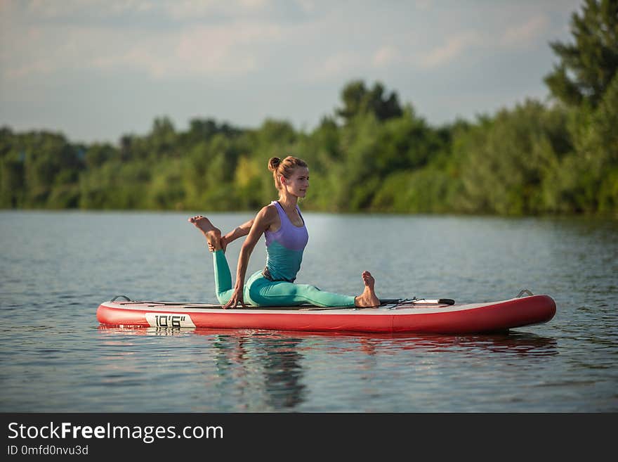 Young woman doing yoga on sup board with paddle. Meditative pose, side view - concept of harmony with the nature, free and healthy living, freelance, remote business.