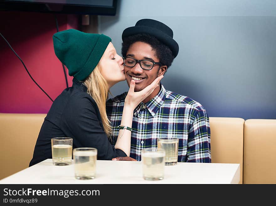 Close-up of girlfriend kissing her smiling boyfriend siting in the restaurant. Close-up of girlfriend kissing her smiling boyfriend siting in the restaurant