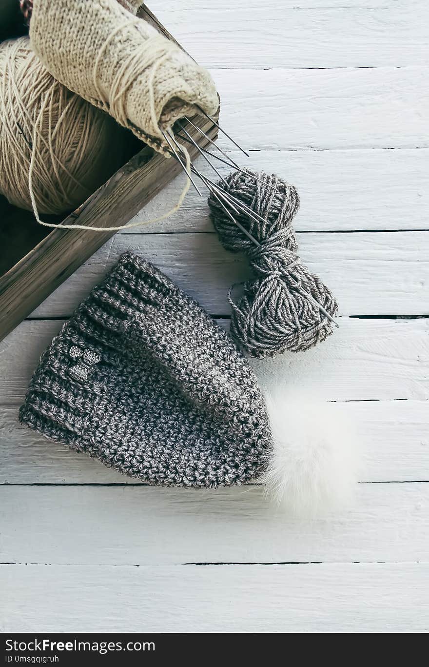 Knitted warp wainter cap with fluffy pompon and woolen grey yarn on white wooden background