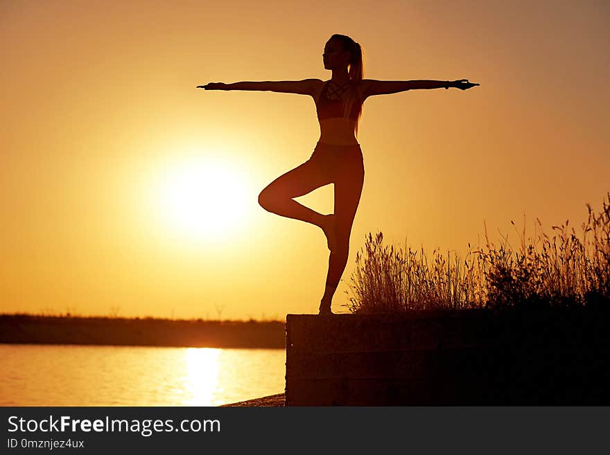 Silhouette woman practicing yoga or stretching on the beach pier at sunset or sunrise.