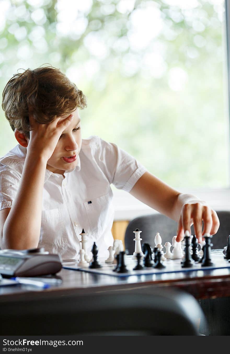 Cute handsome boy in white t shirt plays chess with his rival in chess class. Education concept, intellectual game.