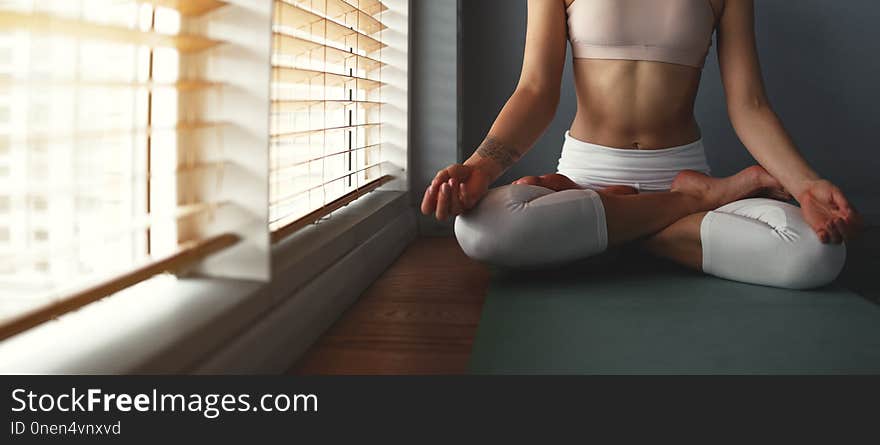 Young woman practices yoga at gym by the window