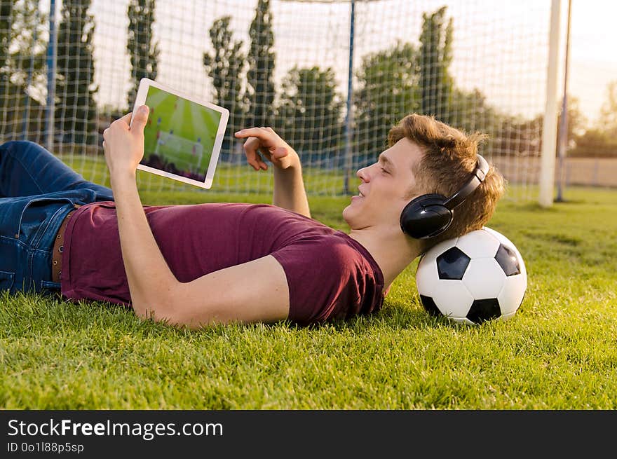 Teenager laying on grass with soccer ball behind his neck