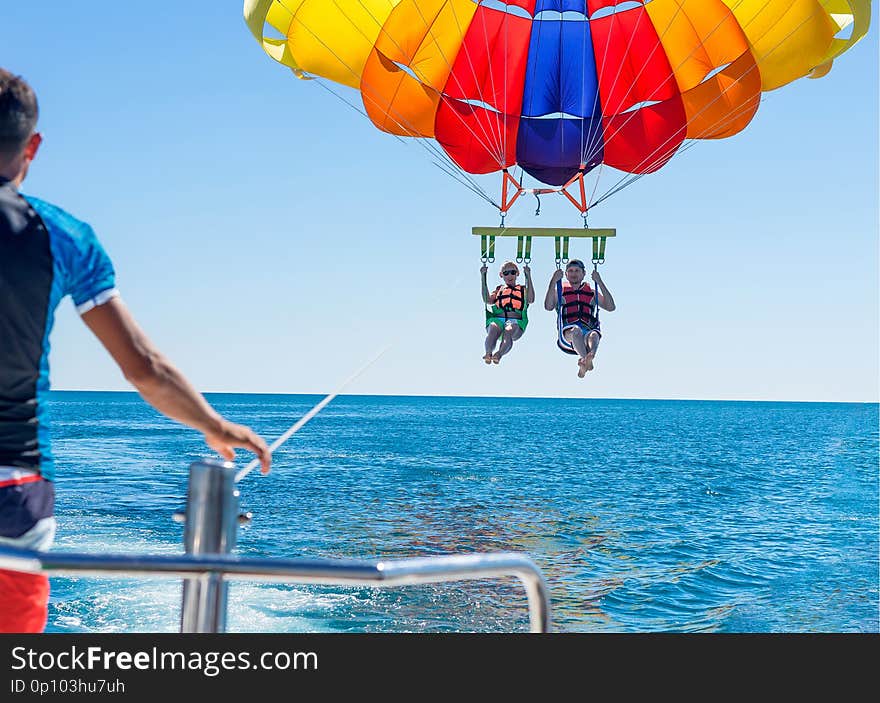 Happy couple Parasailing on Miami Beach in summer. Couple under parachute hanging mid air. Having fun. Tropical Paradise. Positive