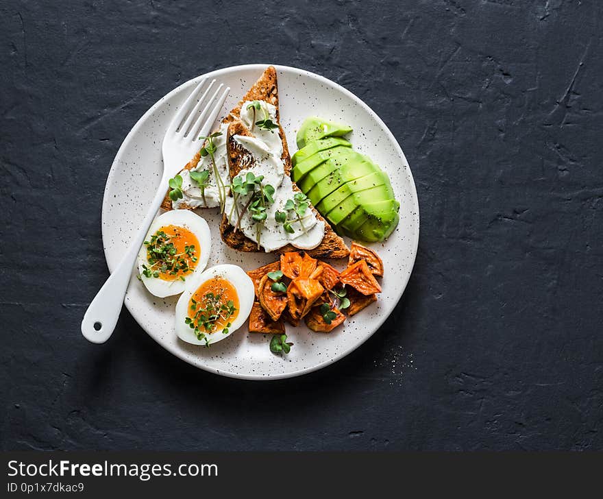 Cream cheese toast, avocado, boiled egg, baked sweet potatoes - delicious healthy breakfast or snack on a dark background