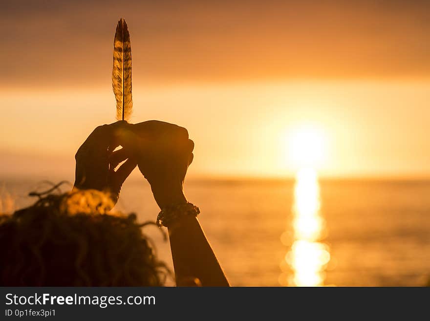 Woman hands taking a feather in front of an amazing golden and hot sunset over the sea. vacation and freedom independence concept. enjoying nature and feeling the world. conceptual image with weight and life