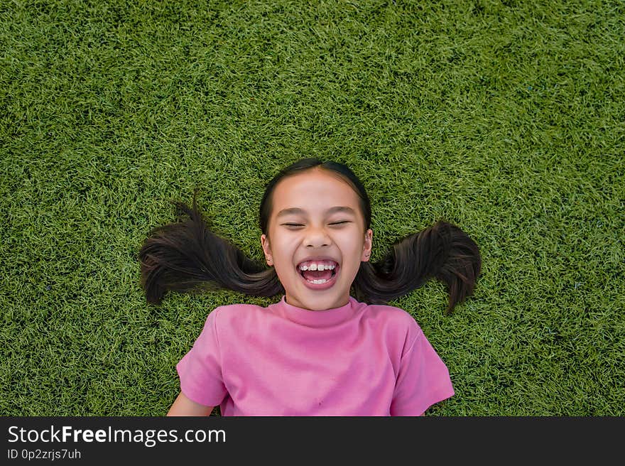 Kid asian girl`s lie leisurely on the Lawn floor and smile looking at