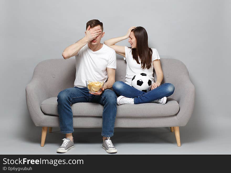 Displeased couple woman man football fans cheer up support favorite team with soccer ball, holding bowl of chips