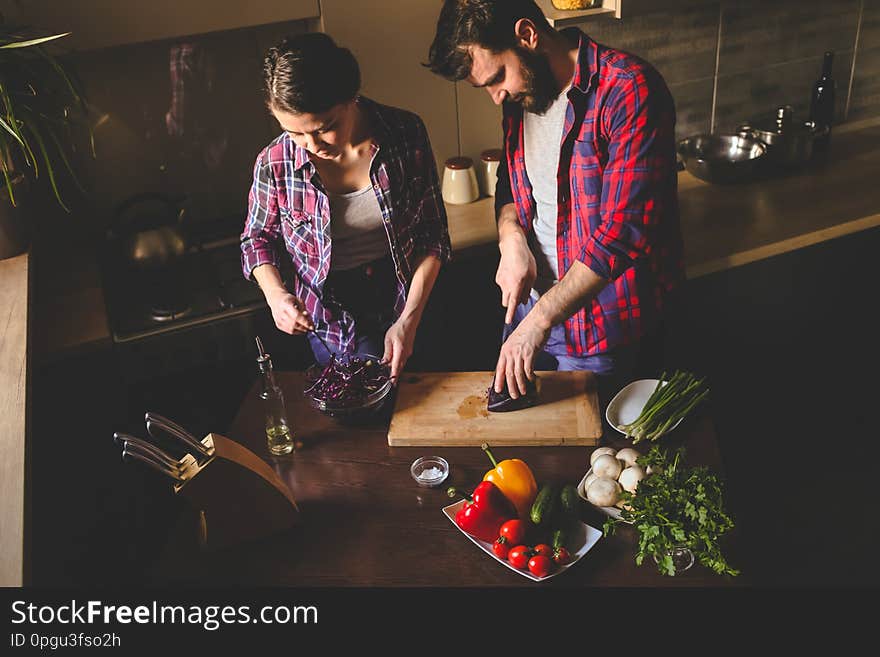 Beautiful young couple in kitchen at home while cooking healthy food. Husband cut cabbage. Wife mix salad. Scene from family life. Horizontally framed shot