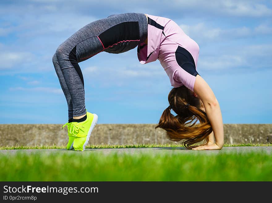 Super fit attractive young woman wearing fashionable outfit working out being active outside during sunny weather. Stretching her back or practice yoga. Super fit attractive young woman wearing fashionable outfit working out being active outside during sunny weather. Stretching her back or practice yoga