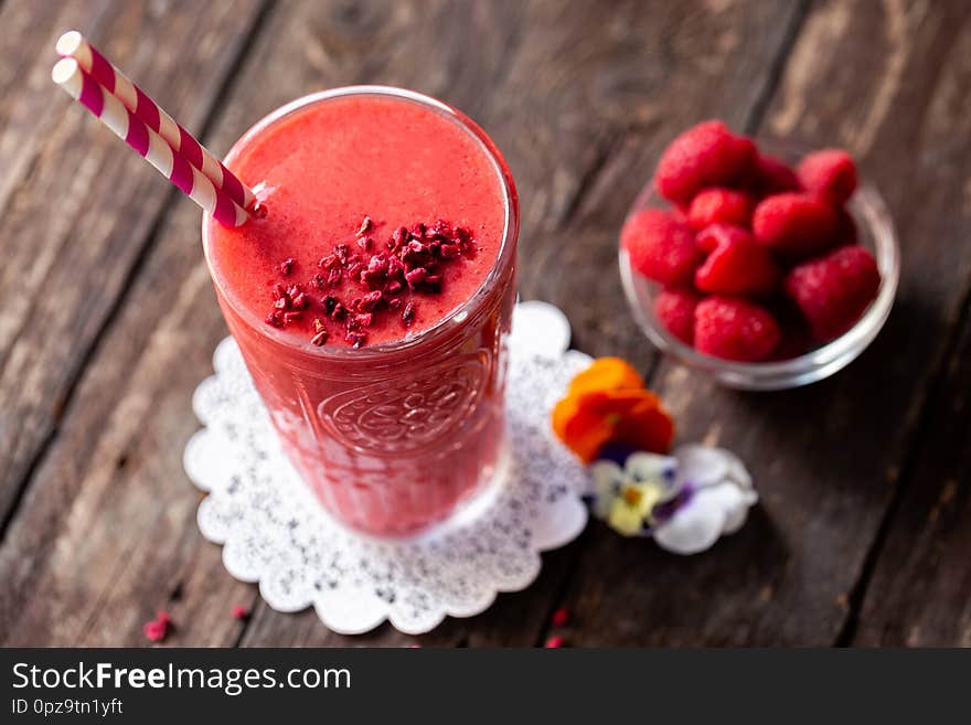 Delicious smoothie made of berries served on the table in glass with two straws in purple-red and white color combination