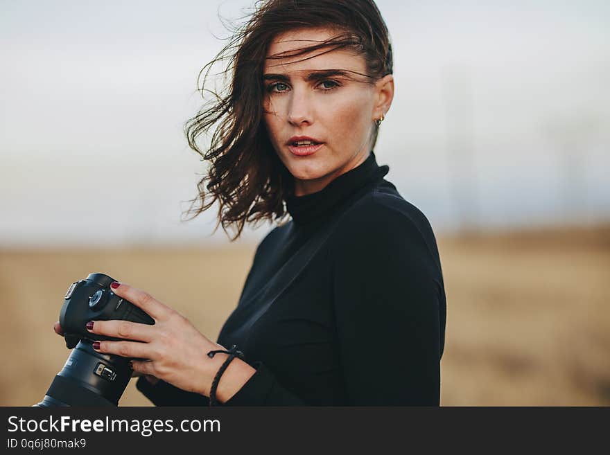 Professional photographer during a outdoors photoshoot. Young woman in casual holding a photo camera outdoors