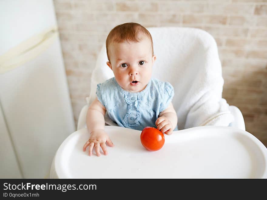 Baby eating vegetables. red tomato in little girl hand in sunny kitchen. Healthy nutrition for kids. Snack or breakfast for young