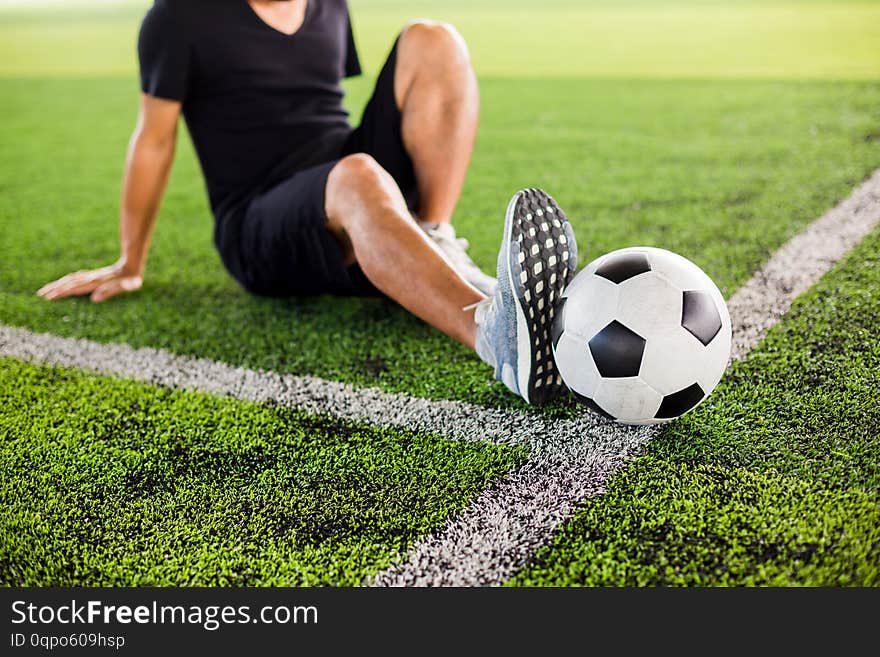 Soccer ball on green artificial turf with the player is stretch the muscles