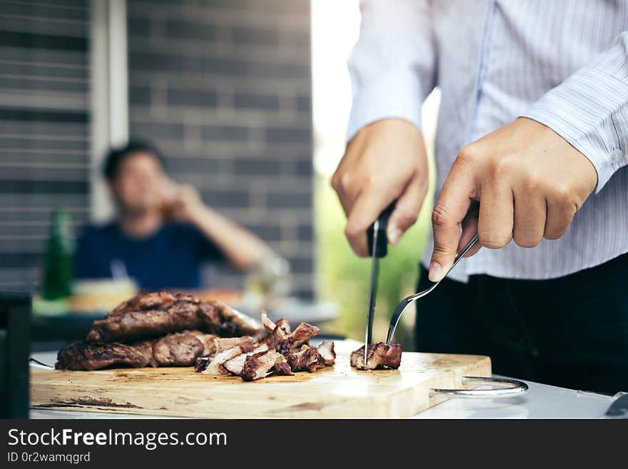 Asian friends are using a knife and a fork to cut the grilled meat on the chopping board to bring food together with friends celebrate with fun.