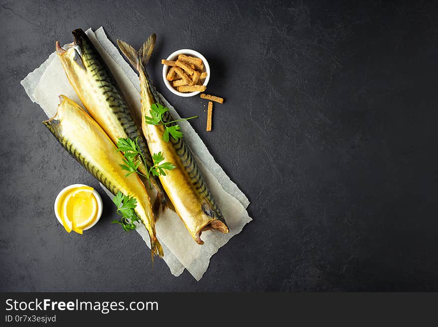 Smoked fish mackerel or scomber on a white parchment paper. Black or dark stone background. Top view. Smoked fish mackerel or scomber on a white parchment paper. Black or dark stone background. Top view