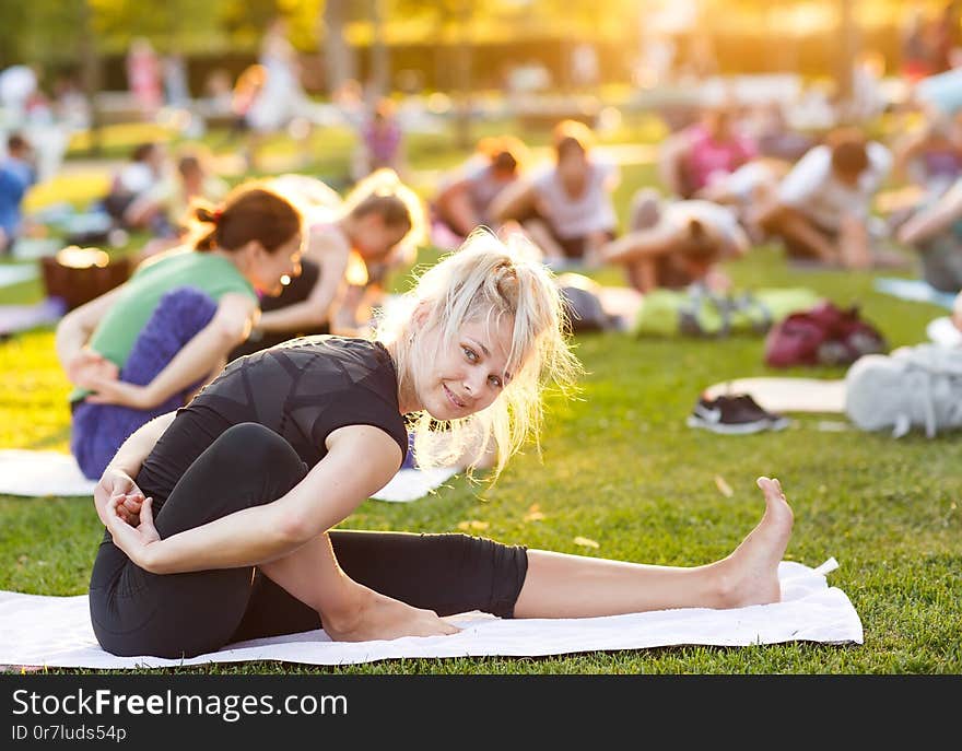 Big group of adults attending a yoga class outside in park.