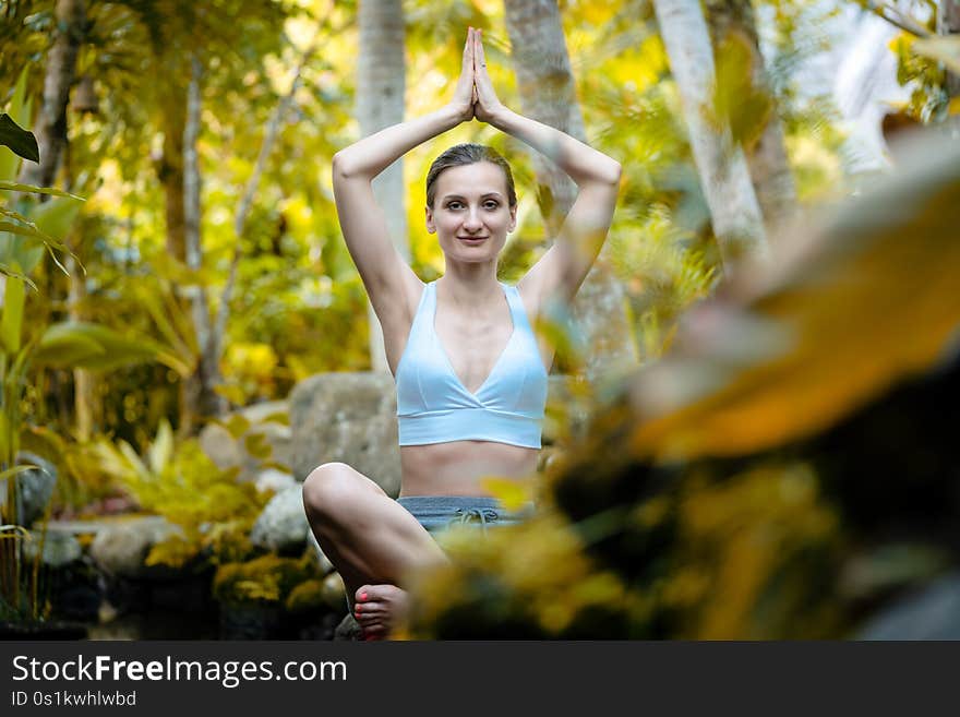 Woman doing yoga in the tropical jungle sitting on a stone