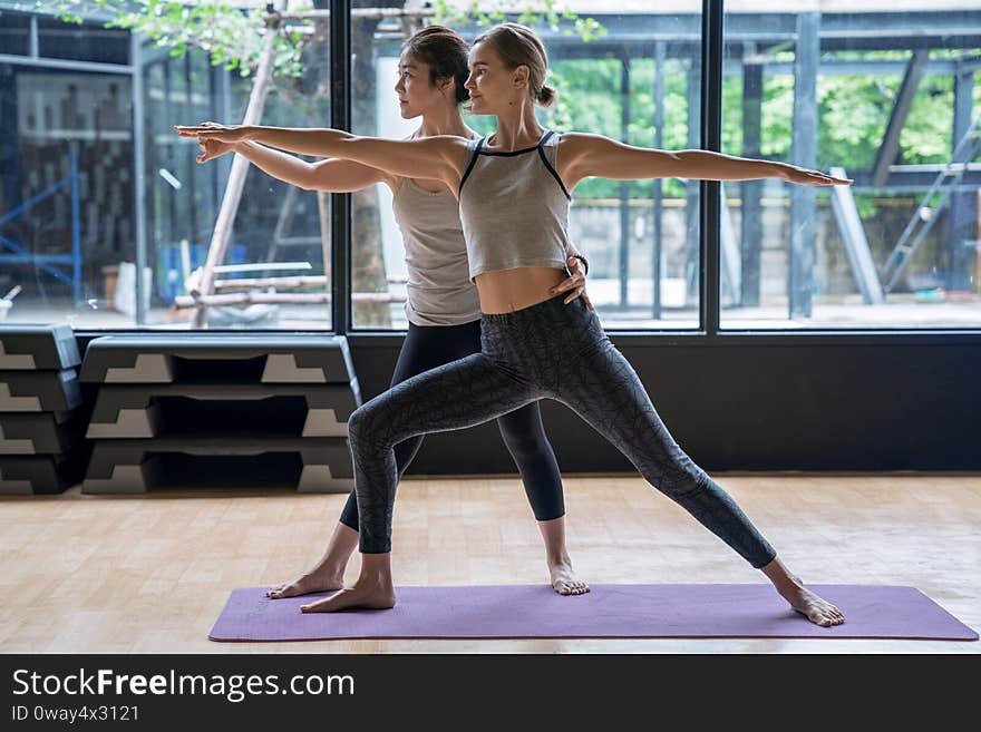 The trainer adjusts the correct posture for the student to learn yoga at fitness club.