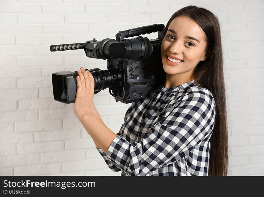 Operator with professional video camera near white brick wall