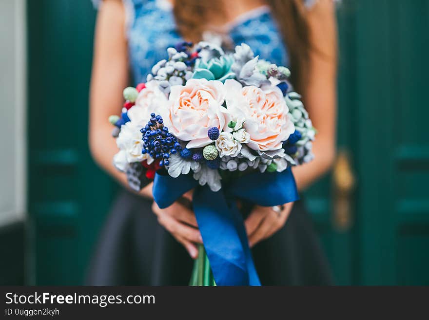 Elegant female hands holding handmade flowers made from Japanese polymer clay. They look like a real wedding bouquet. Against the background of a green wooden door.