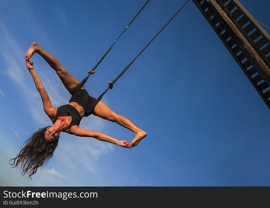 Aero yoga workout - young attractive and athletic woman practicing aerial yoga exercise training acrobatic  body postures isolated on blue sky in balance flexibility control and healthy lifestyle