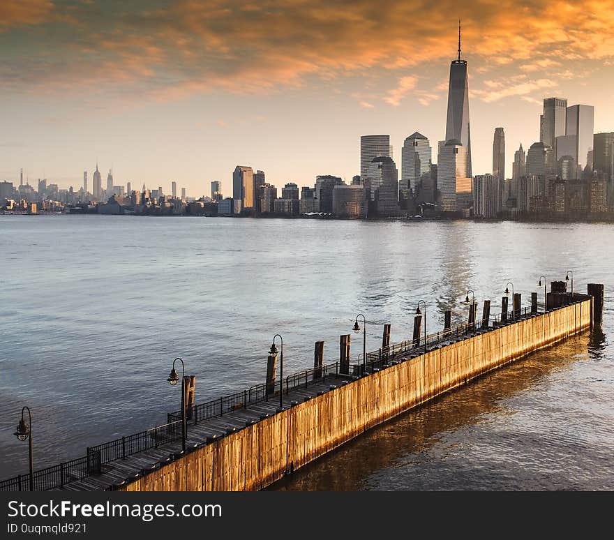 The warmth and comfort of the early morning sun is captivating in this aerial view of the New York City skyline from Hoboken NJ. The sun accentuates the pier and the sky with beautiful orange light. The warmth and comfort of the early morning sun is captivating in this aerial view of the New York City skyline from Hoboken NJ. The sun accentuates the pier and the sky with beautiful orange light.