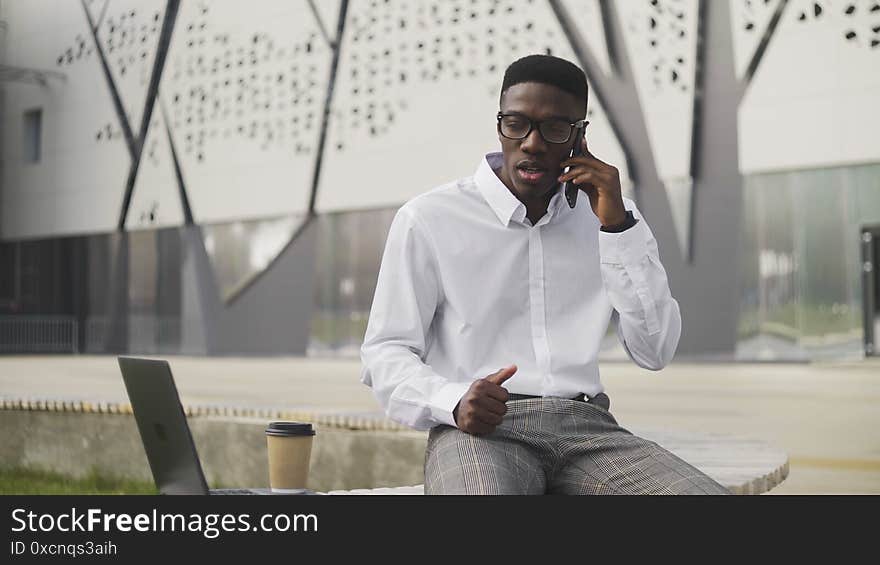 Serious African Businessman with glasses talking on cell phone in city park 4K