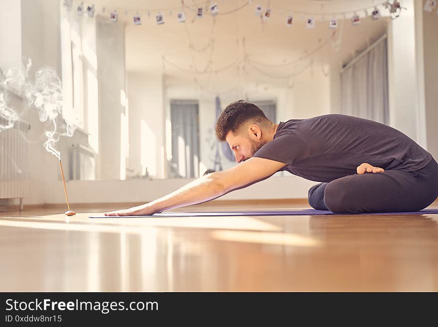 Handsome male practicing yoga while sitting on the floor with incense stick. Handsome male practicing yoga while sitting on the floor with incense stick