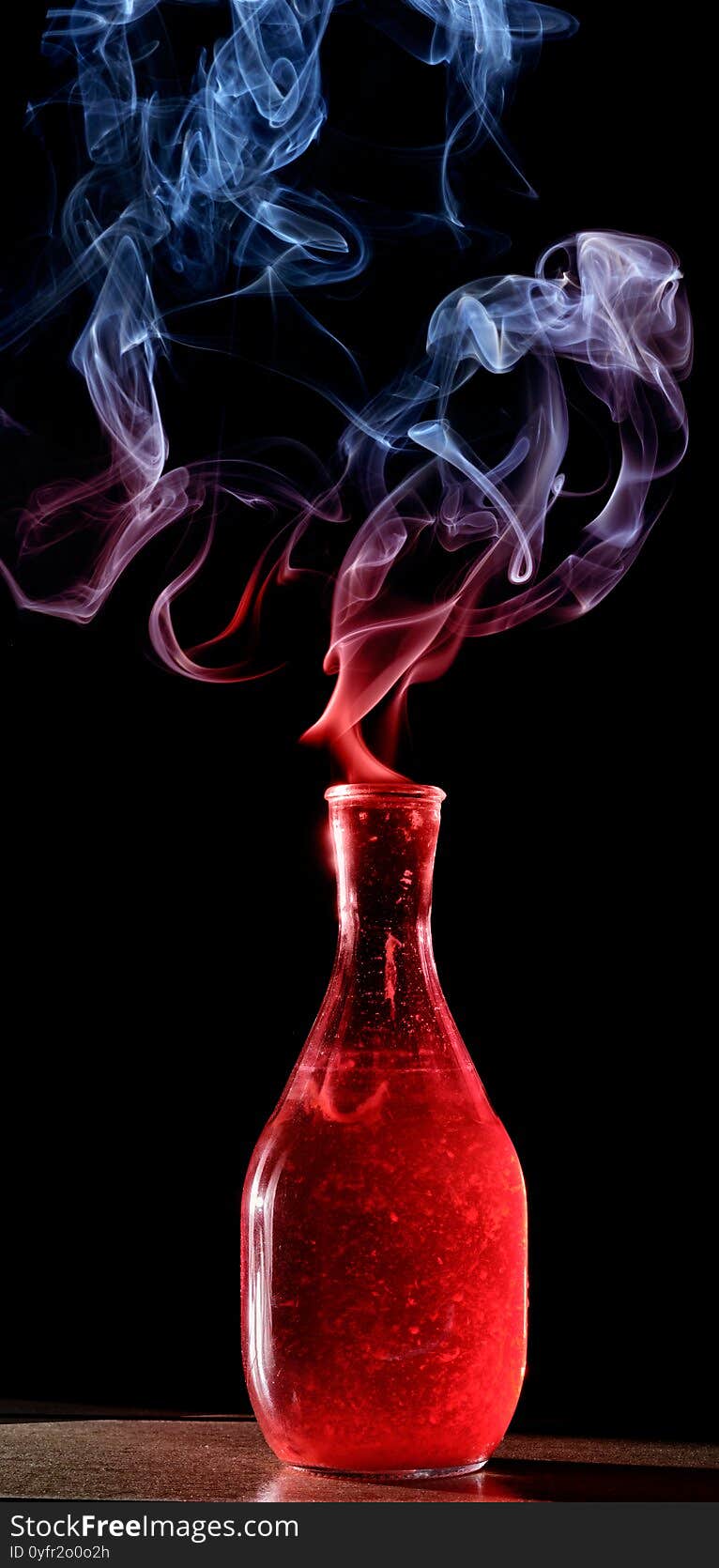 One magic bottle of red liquor coming out of colored smoke. One magic bottle of red liquor coming out of colored smoke