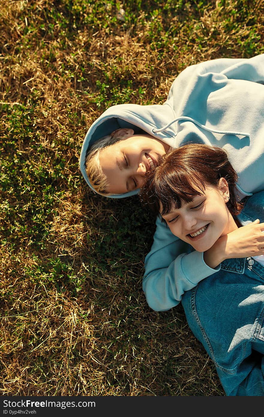 Top view of happy lesbian couple of girls lying on the grass in summer park, women in love laughing, spending time