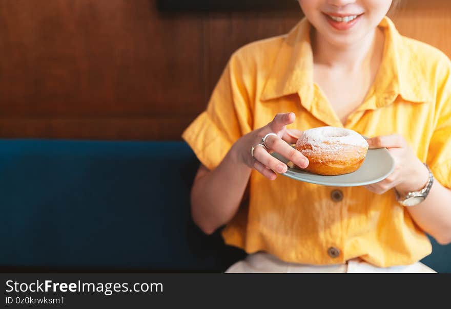 Woman smile and wearing yellow shirt holding and showing a pale green plate of sugar glazed donut in a modern cafe.