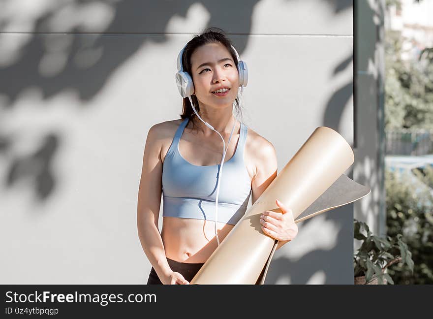 Asian healthy and sportive woman listening music and holding yoga mat after finish class at gym. Asian healthy and sportive woman listening music and holding yoga mat after finish class at gym